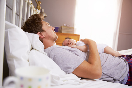 Father Sleeping In Bed Holding Newborn Baby Daughterの写真素材