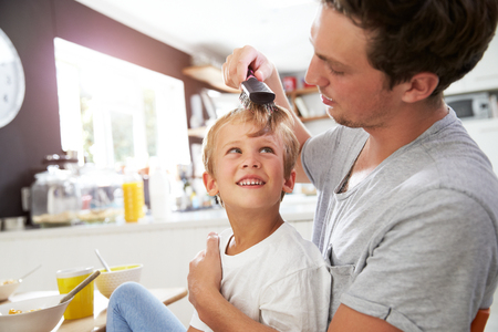 Father Brushing Son's Hair At Breakfast Tableの写真素材