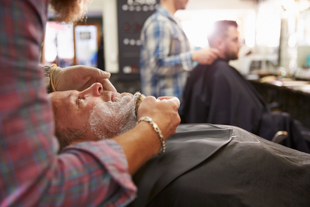 Male Barber Preparing Client For Shave In Shopの写真素材