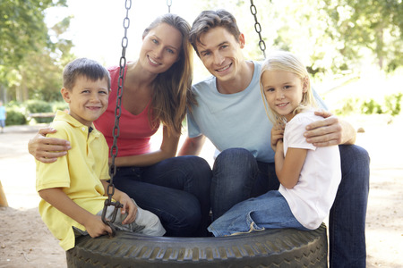 Family Sitting On Tyre Swing In Playgroundの写真素材
