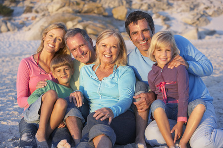 Three Generation Family On Holiday Sitting On Beach