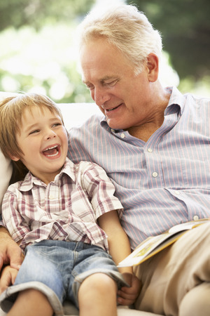 Grandfather With Grandson Reading Together On Sofaの写真素材