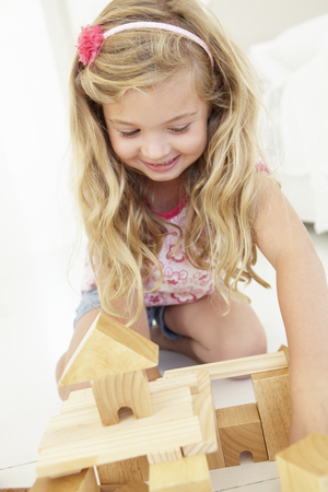 Young Girl Playing With Wooden Building Blocks In Bedroomの写真素材