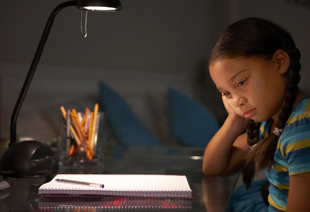 Unhappy Young Girl Studying At Desk In Bedroom In Eveningの写真素材