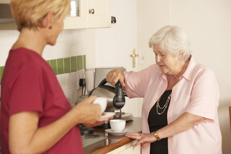 Home Help Sharing Cup Of Tea With Senior Woman In Kitchenの写真素材