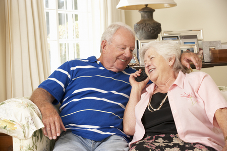 Retired Senior Couple Sitting On Sofa Talking On Phone At Home Togetherの写真素材