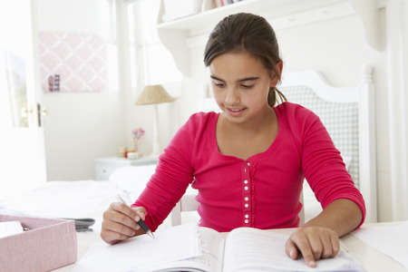 Young Girl Doing Homework At Desk In Bedroomの写真素材
