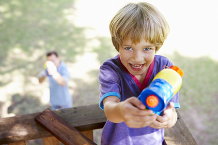 Father And Son Having Water Pistol Fight In Tree Houseの写真素材