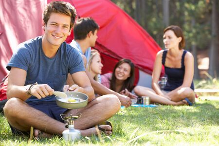Young Man Cooking Breakfast For Friends On Camping Holidayの写真素材