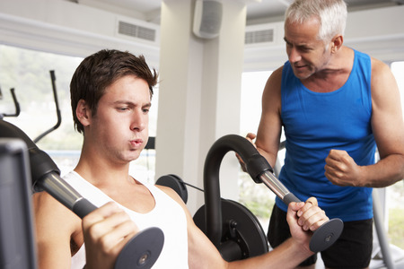 Middle Aged Man Being Encouraged By Personal Trainer In Gymの写真素材
