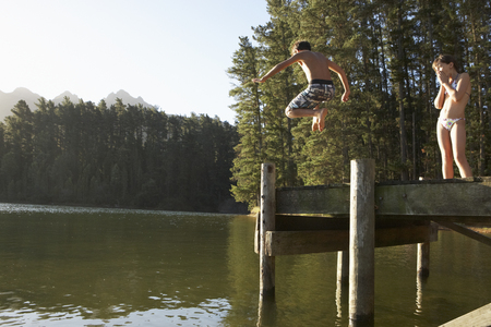 Two Children Jumping From Jetty Into Lakeの写真素材