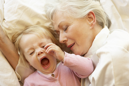 Grandmother Cuddling Granddaughter In Bedの写真素材