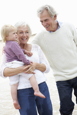 Grandparents And Granddaughter Walking Along Beach Togetherの写真素材