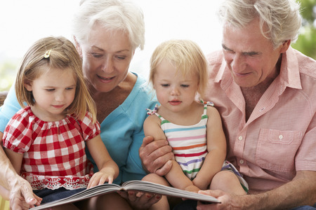 Grandparents And Grandchildren Reading Book On Garden Seatの写真素材