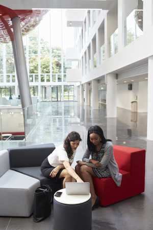 Two Businesswomen Using Laptop In Lobby Of Modern Officeの写真素材