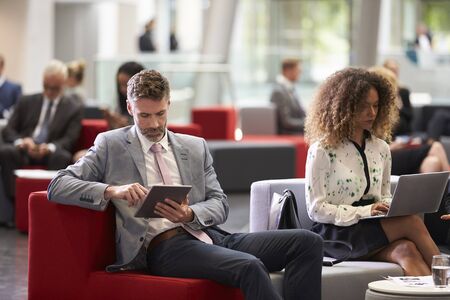 Businesspeople Using Digital Devices In Busy Office Lobbyの写真素材