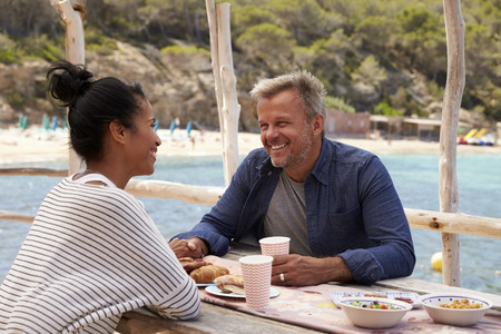 Middle aged couple smiling across a table by the sea, Ibizaの写真素材