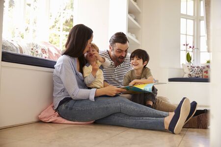 Family Sitting On Floor Reading Story At Home Together