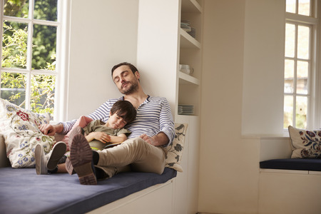 Father And Son Sleeping On Window Seat At Home Togetherの写真素材