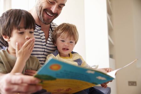 Close Up Of Father And Sons Reading Story At Home Togetherの写真素材