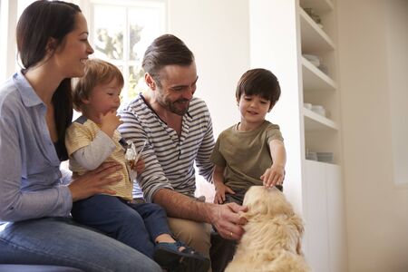 Family Sitting On Window Seat At Home With Golden Retrieverの写真素材