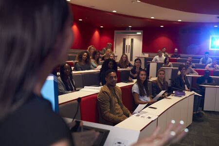 Woman lecturing students in lecture theatre, focus midground