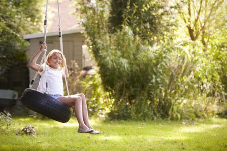 Portrait Of Young Girl Playing On Tire Swing In Gardenの写真素材