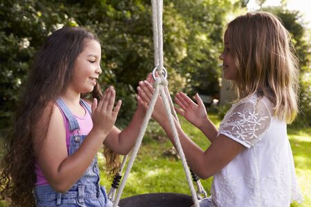 Two Girls Sitting On Swing Playing Clapping Gameの写真素材