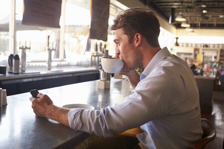 Man Checking Messages On Phone In Coffee Shopの写真素材