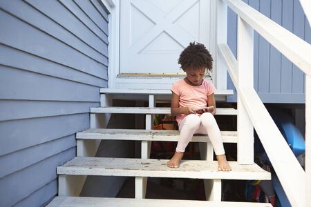 Young Girl Sits On Outdoor Steps Playing With Mobile Phone