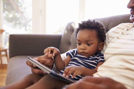 Father And Son Sitting On Sofa At Home Using Digital Tablet