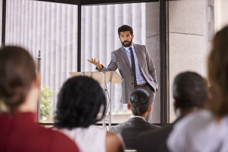 Hispanic man presenting business seminar leaning on lecternの写真素材