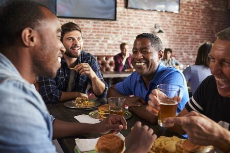 Male Friends Eating Out In Sports Bar With Screens In Behindの写真素材