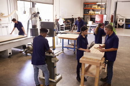 Carpenters Working On Machines In Busy Woodworking Workshop