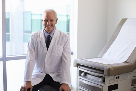 Portrait Of Male Doctor Wearing White Coat In Exam Roomの写真素材