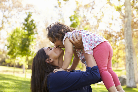 Mixed race Asian mum kissing her young daughter in parkの写真素材
