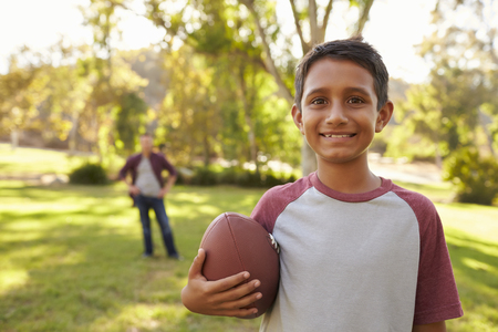 Portrait of boy holding football in park, dad in backgroundの写真素材