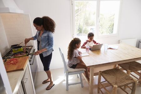 Mum cooking while kids work at kitchen table, elevated viewの写真素材