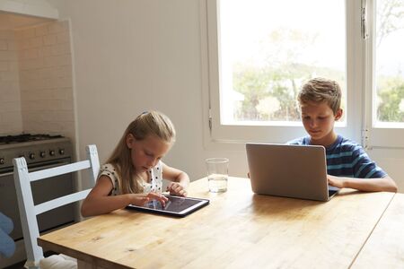 Children At Home Using Digital Devices On Kitchen Tableの写真素材