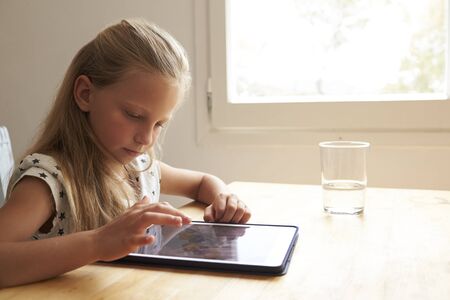 Young Girl At Home Using Digital Tablet On Kitchen Tableの写真素材