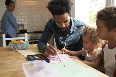 Children And Father Painting Picture On Kitchen Tableの写真素材