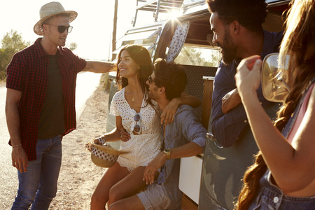 Friends on a road trip relax beside their camper van