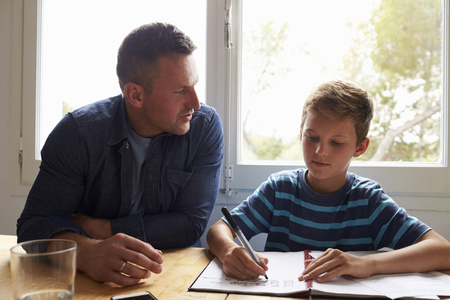 Father Helping Son With Homework Sitting At Kitchen Tableの写真素材