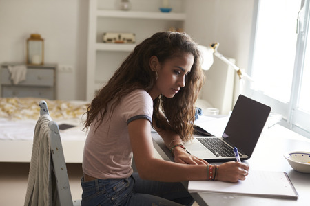 Teenage girl doing homework at a desk in her bedroom