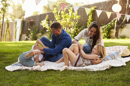 Parents Playing Game With Children On Blanket In Gardenの写真素材
