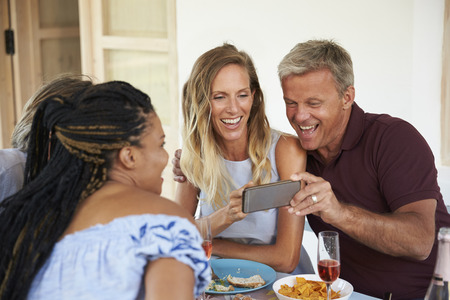 Friends at a dinner table look at pictures on a smartphoneの写真素材