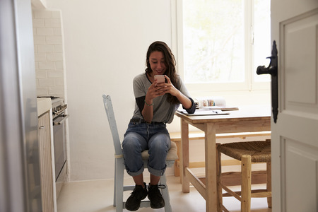 View from doorway of girl messaging on smartphone in kitchen