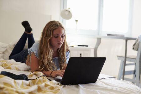 Teenage girl using laptop lying on her bedの写真素材