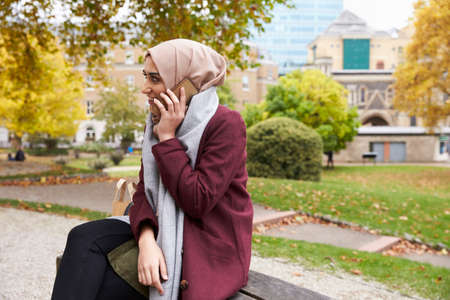 British Muslim Woman On Break Using Mobile Phone In Parkの写真素材