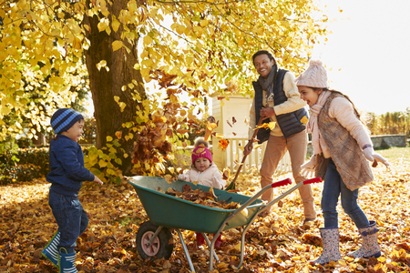 Children Helping Father To Collect Autumn Leaves In Garden Children Helping Father To Collect Autumn Leaves In Garden